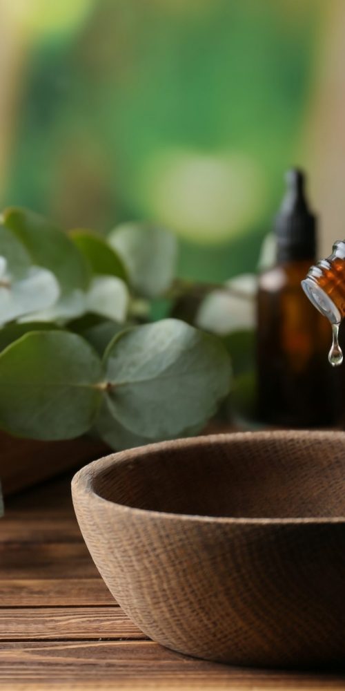 Woman pouring eucalyptus essential oil into bowl on&nbsp;wooden table